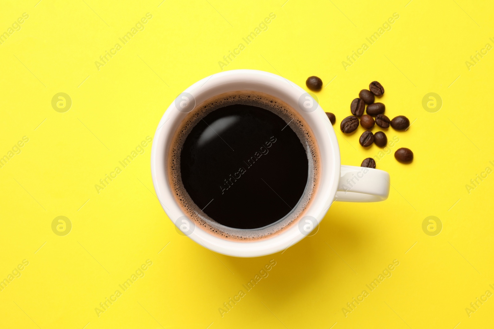 Photo of Fresh coffee in cup and roasted beans on yellow background, top view