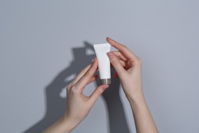 Photo of Woman holding tube of cream on grey background, closeup