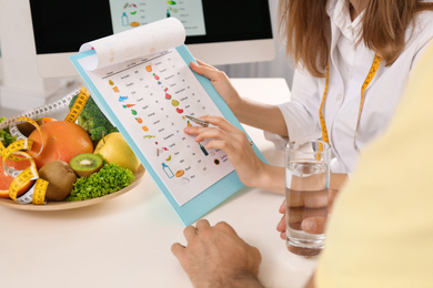 Young nutritionist consulting patient at table in clinic, closeup