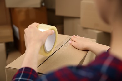 Photo of Woman taping cardboard box indoors, closeup view