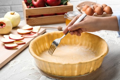 Photo of Woman making holes in raw dough with fork at white wooden table, closeup. Baking apple pie