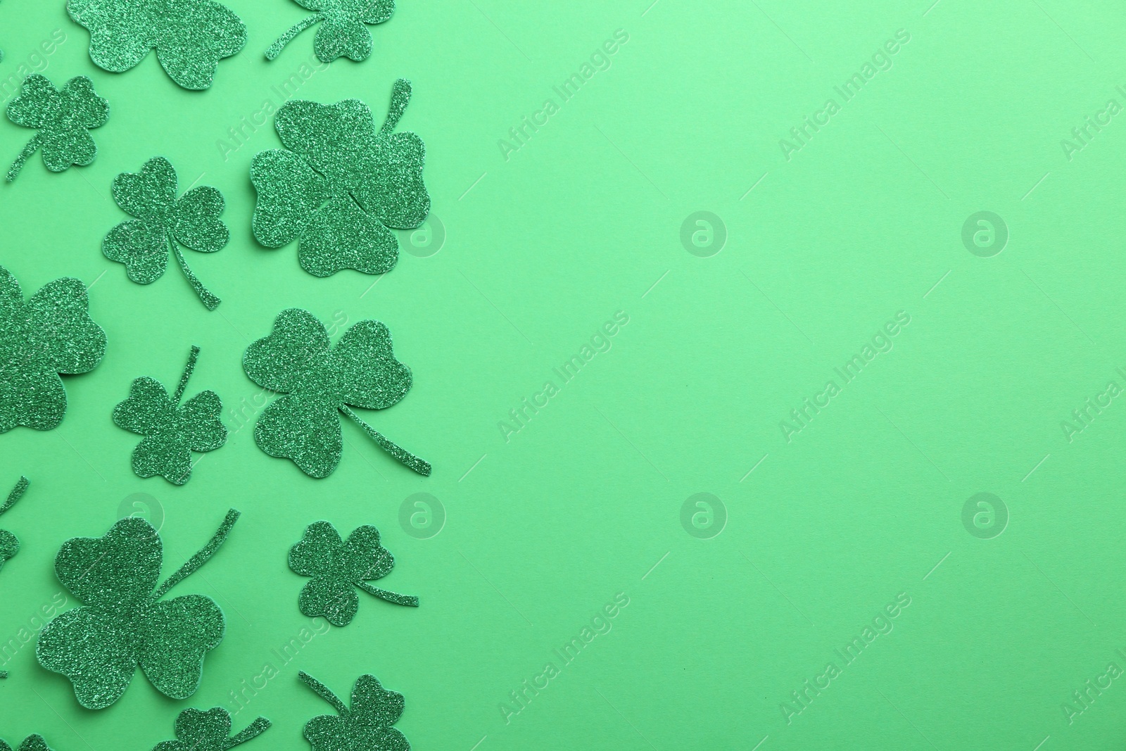 Photo of St. Patrick's day. Shiny decorative clover leaves on green background, flat lay. Space for text