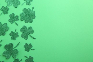 St. Patrick's day. Shiny decorative clover leaves on green background, flat lay. Space for text