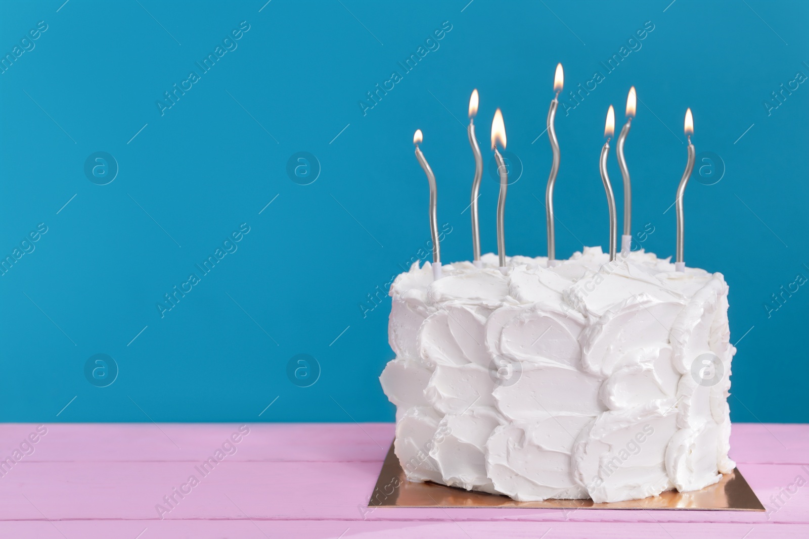 Photo of Delicious cake with cream and burning candles on pink wooden table. Space for text