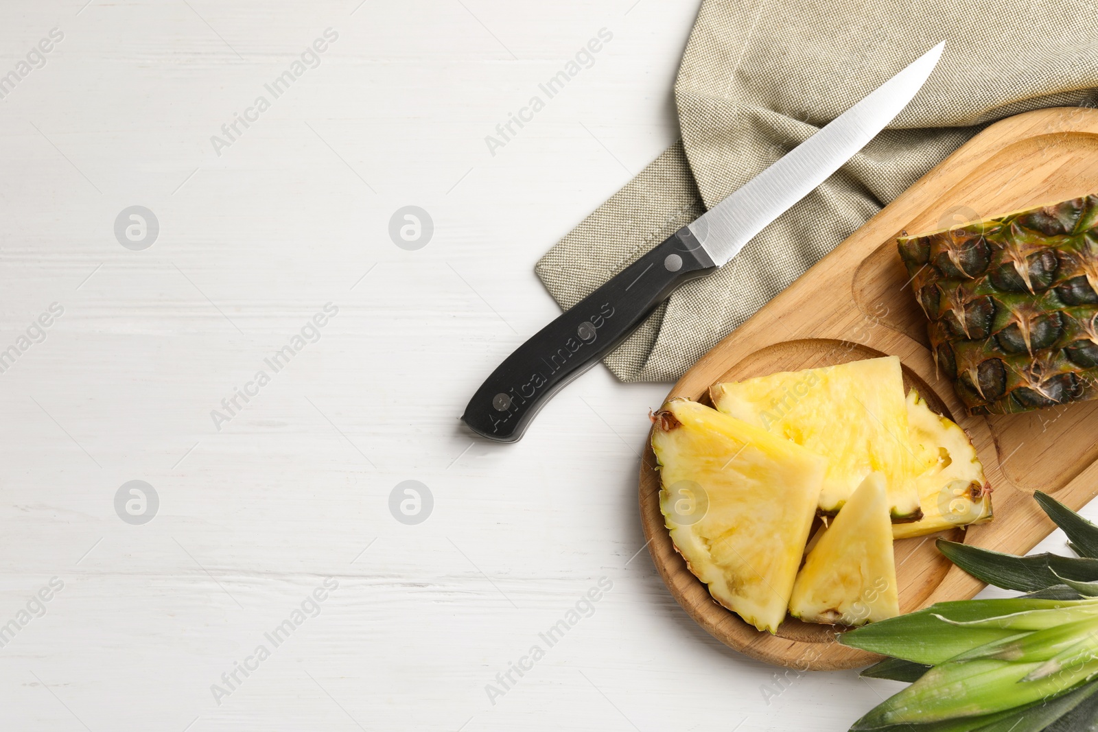 Photo of Slices of ripe juicy pineapple and knife on white wooden table, flat lay. Space for text