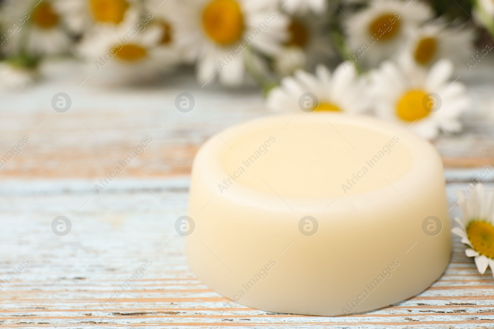 Photo of Solid shampoo bar and chamomiles on light wooden table, closeup. Space for text