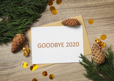Card with text Goodbye 2020 and festive decor on wooden background, flat lay
