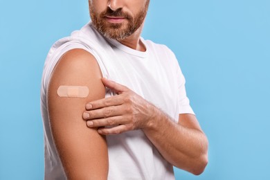 Photo of Man with sticking plaster on arm after vaccination against light blue background, closeup