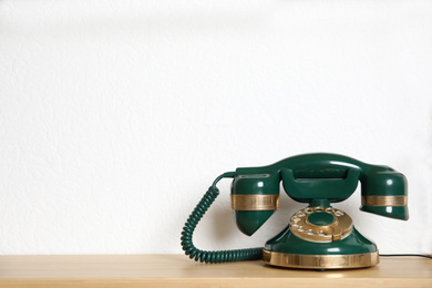 Green vintage corded phone on wooden shelf near white wall. Space for text