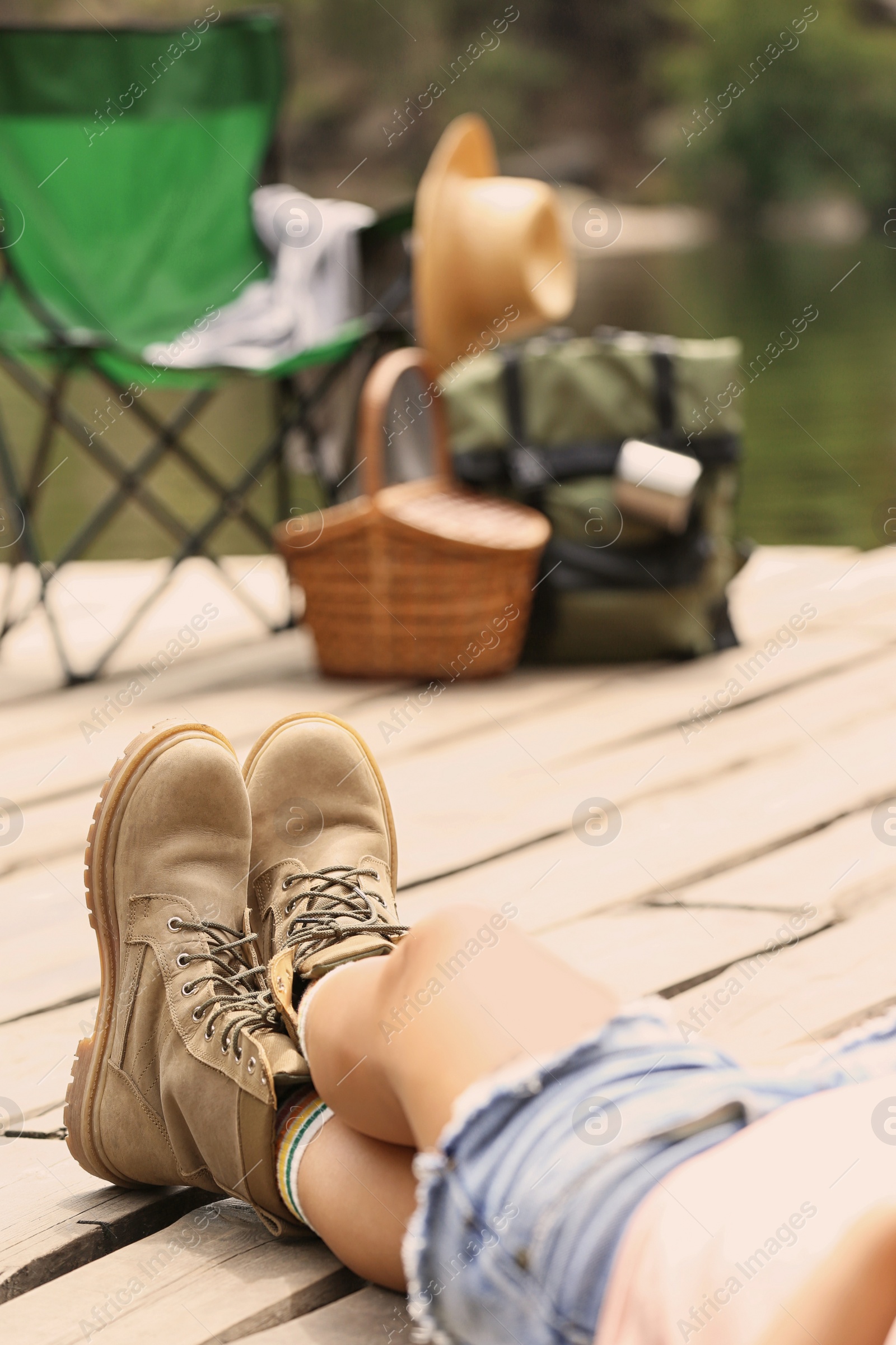 Photo of Woman resting near camping equipment on wooden pier, focus on legs