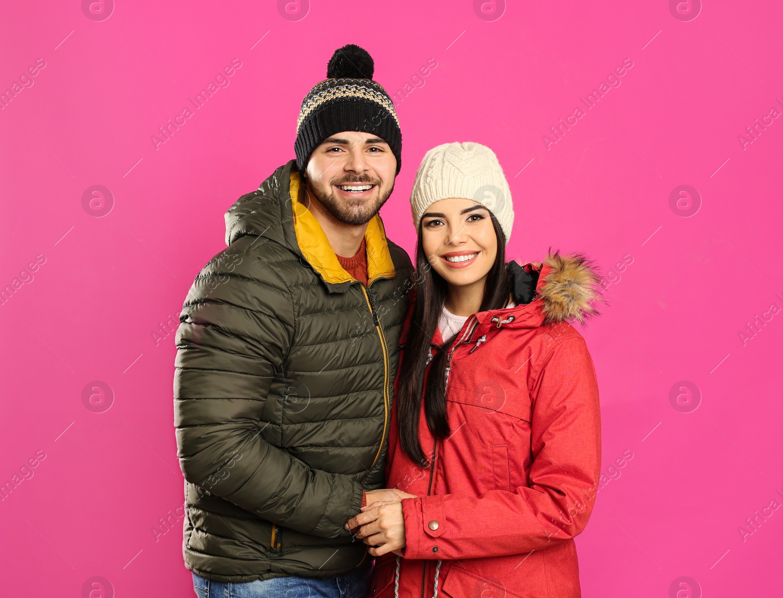 Photo of Happy young couple in warm clothes on pink background. Winter vacation