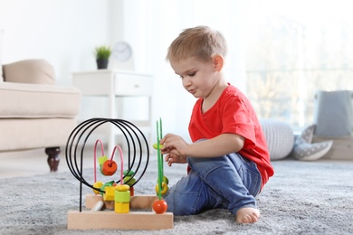 Cute child playing with bead maze on floor indoors