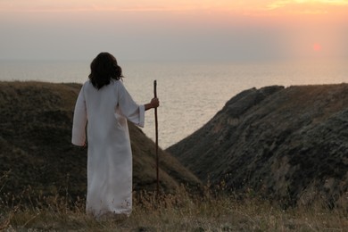Photo of Jesus Christ with stick on hills at sunset, back view. Space for text