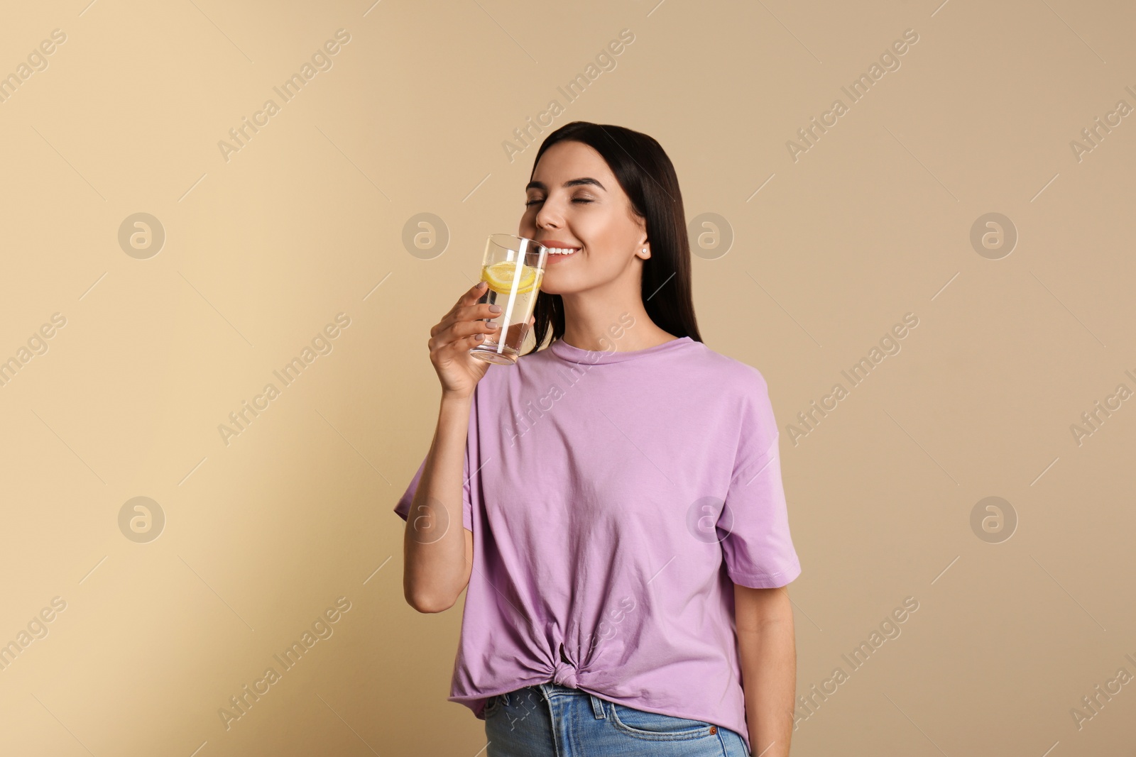 Photo of Beautiful young woman drinking tasty lemon water on beige background