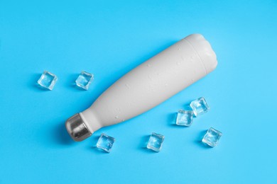 Photo of Stylish thermo bottle with water drops and ice cubes on light blue background, flat lay