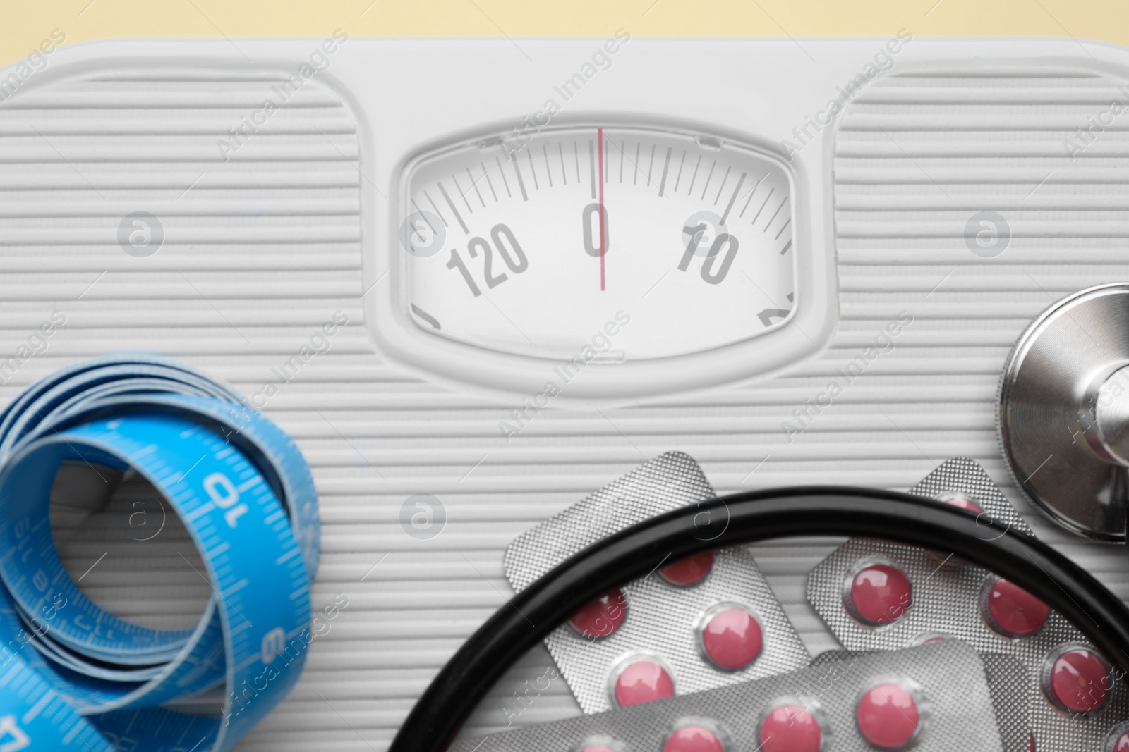 Photo of Scales with weight loss pills, measuring tape, and stethoscope, closeup