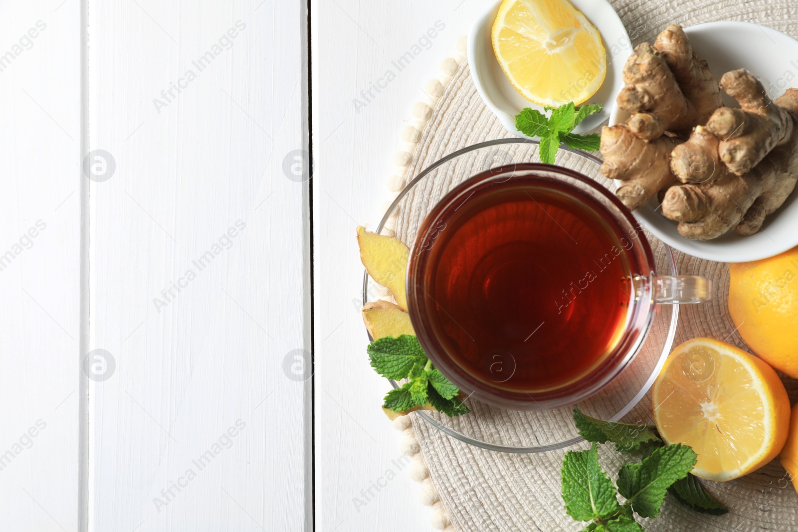 Photo of Cup of delicious ginger tea, mint leaves and lemons on white wooden table, top view. Space for text