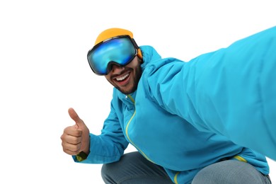 Photo of Smiling young man in ski goggles taking selfie and showing thumbs up on white background