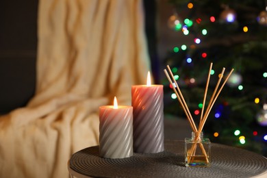 Photo of Aromatic reed air freshener and candles on side table in cozy room