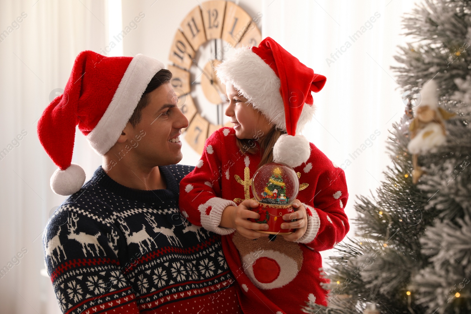 Photo of Father and daughter with snow globe near Christmas tree at home