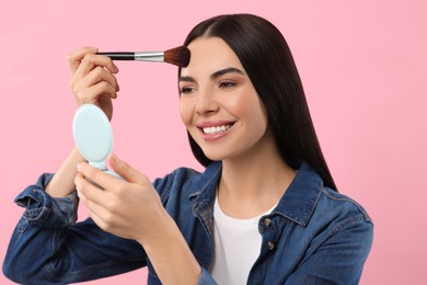 Photo of Beautiful woman with cosmetic pocket mirror applying makeup on pink background