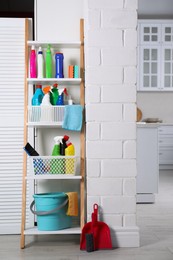 Rack with detergents, cleaning tools and accessories near white wall indoors