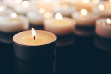 Photo of Wax candles burning on table in darkness, closeup