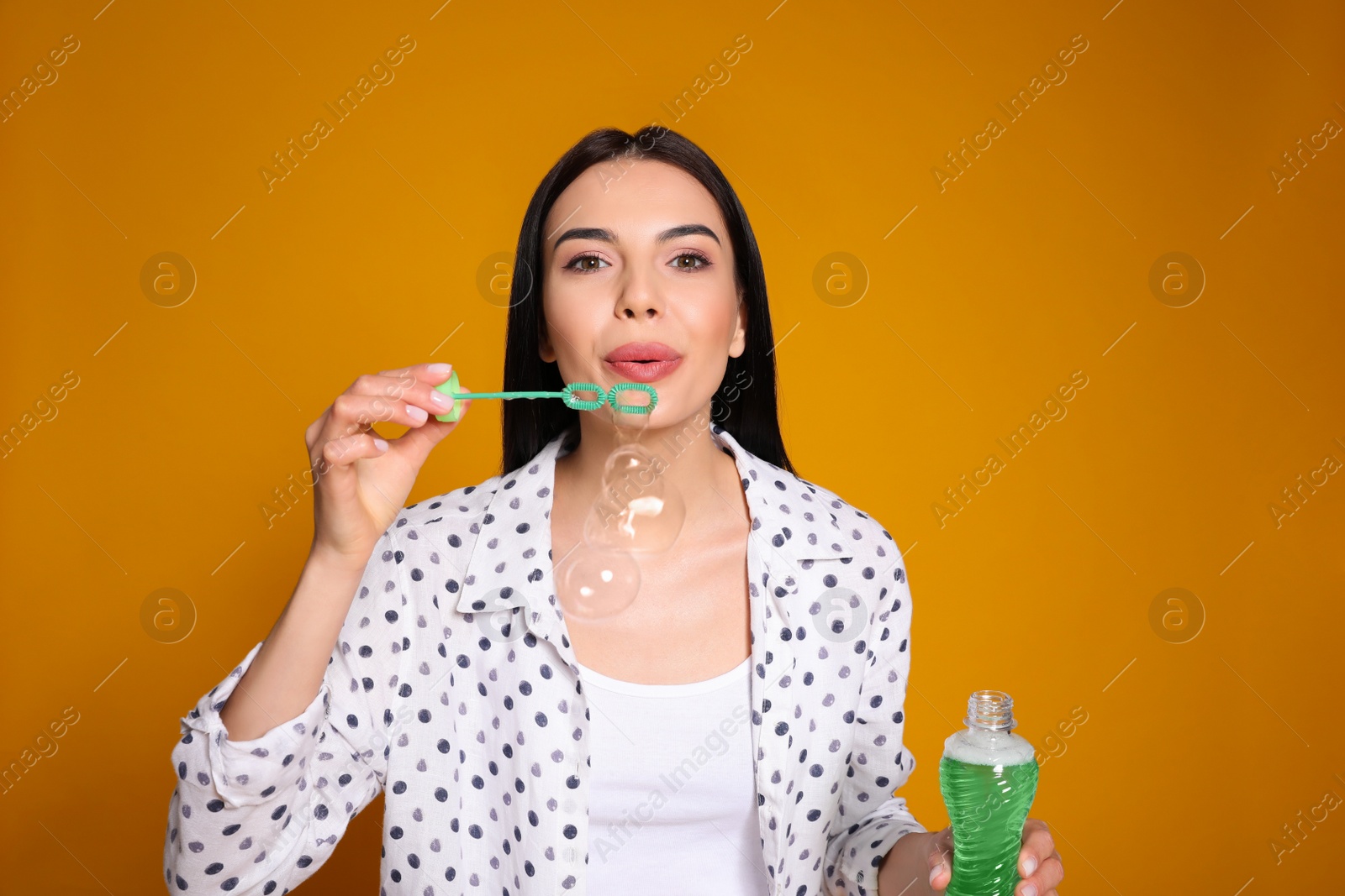 Photo of Young woman blowing soap bubbles on yellow background