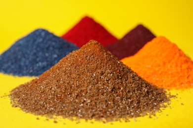 Photo of Heaps of different bright food coloring on yellow background, closeup