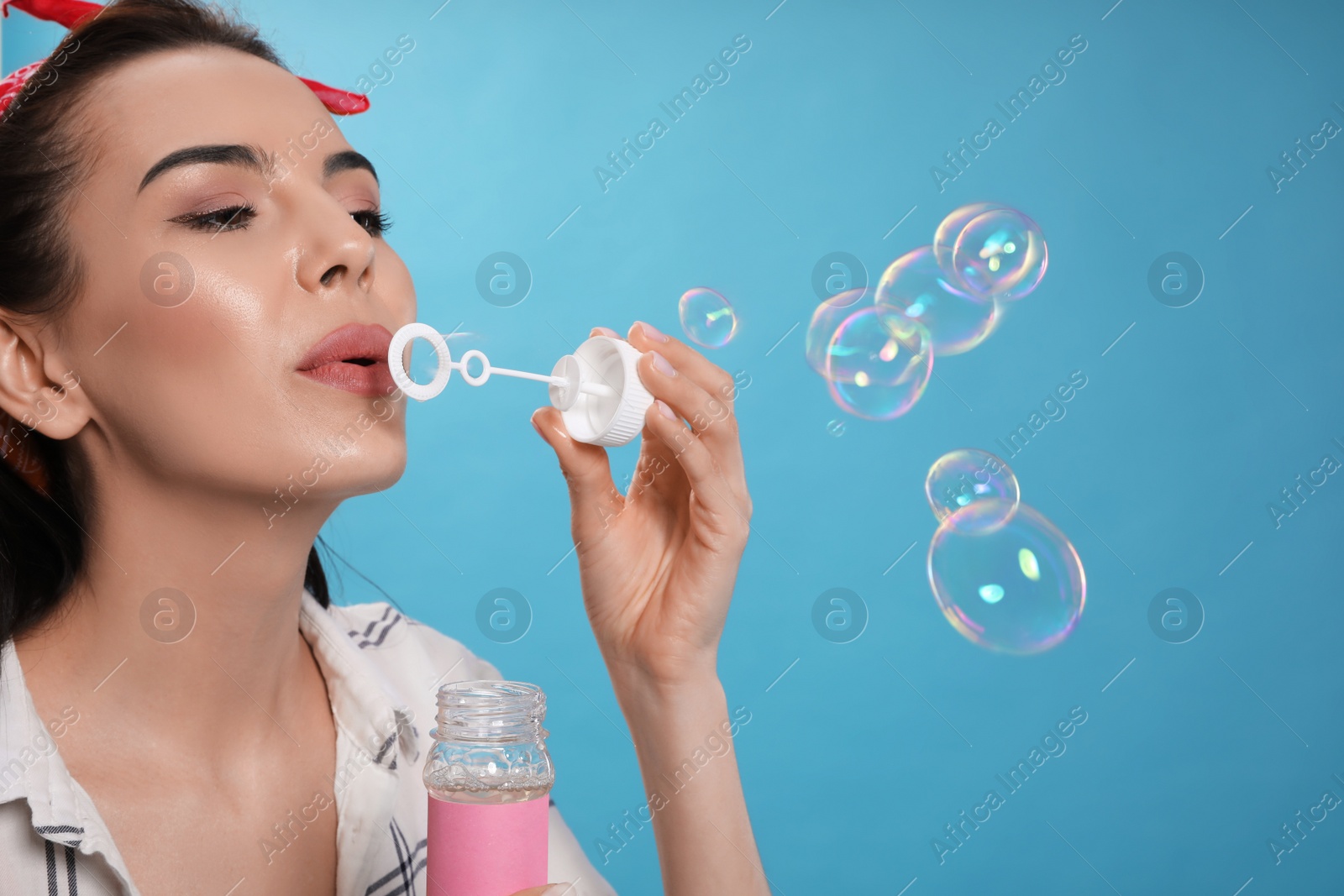 Photo of Young woman blowing soap bubbles on light blue background, space for text