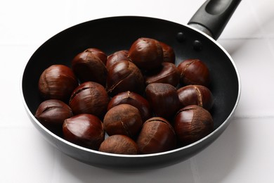 Photo of Fresh edible sweet chestnuts in frying pan on white tiled table