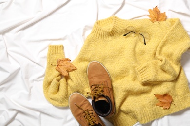 Photo of Flat lay composition with warm sweater and dry leaves on white fabric. Autumn season