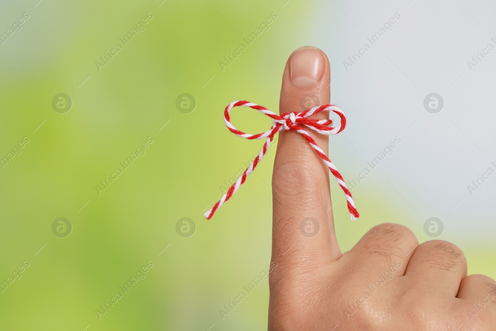 Photo of Man showing index finger with tied bow as reminder on green blurred background, closeup. Space for text