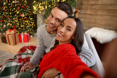 Photo of Happy young couple taking selfie in living room decorated for Christmas