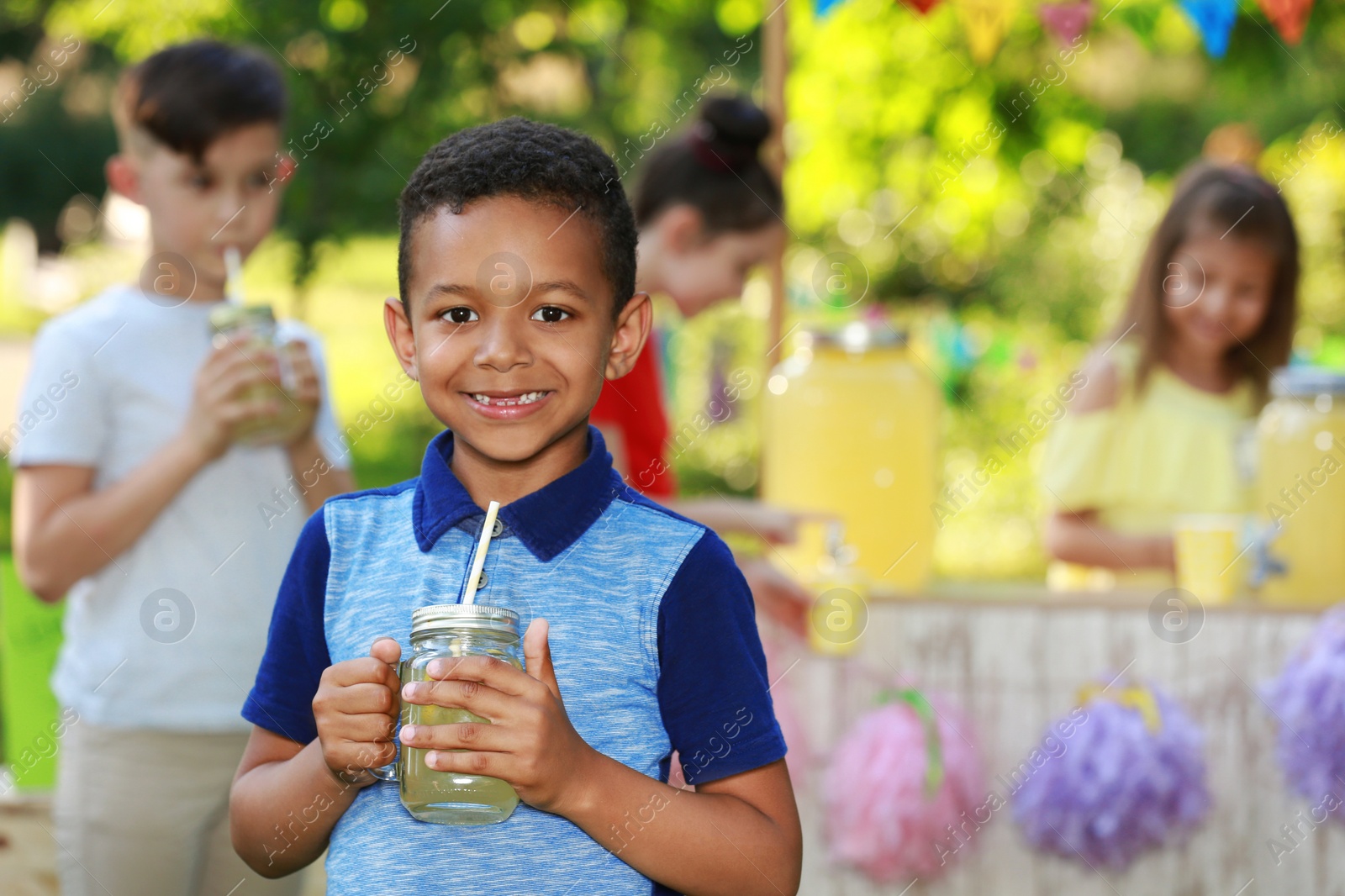 Photo of Cute little African-American boy with natural lemonade in park, space for text. Summer refreshing drink