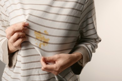 Woman showing shirt with yellow stain on light grey background, closeup