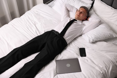 Businessman in office clothes resting on bed indoors