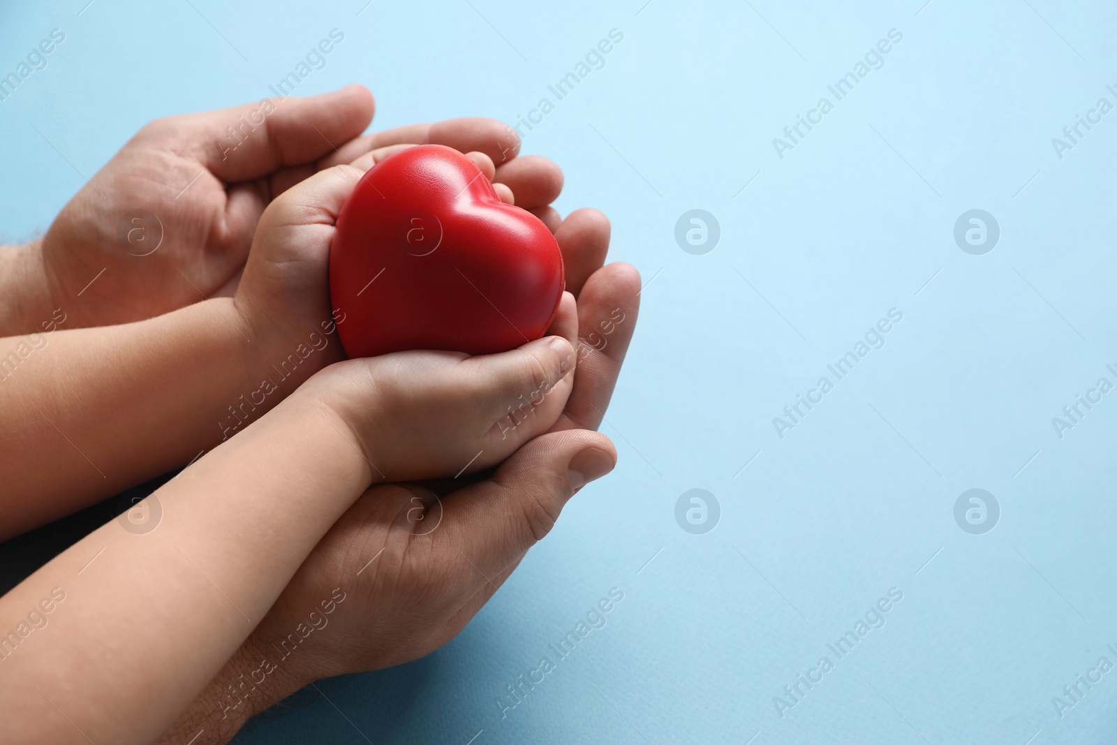 Photo of Father and his child holding red decorative heart on light blue background, closeup. Space for text