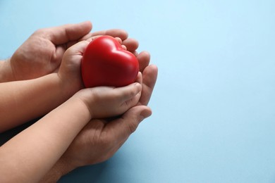 Father and his child holding red decorative heart on light blue background, closeup. Space for text