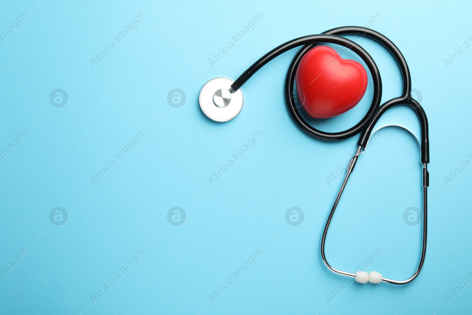 Photo of Stethoscope and red heart on light blue background, top view. Space for text