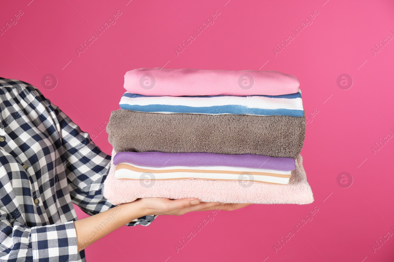 Photo of Young woman holding clean laundry on color background, closeup