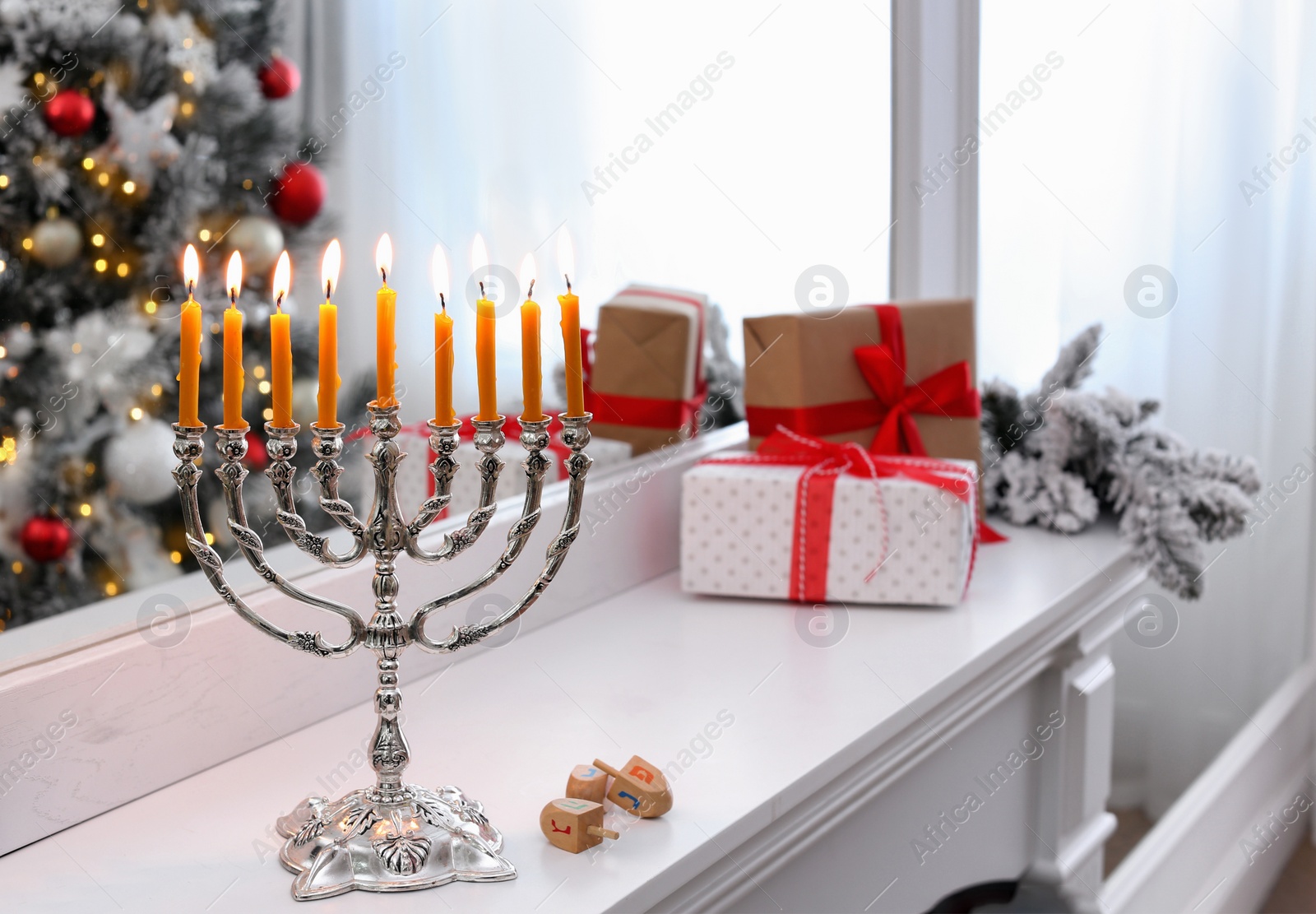 Photo of Silver menorah near dreidels with symbols He, Pe, Nun, Gimel on white mantelpiece in room decorated for Christmas