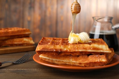 Photo of Pouring honey onto delicious Belgian waffles with butter at wooden table, closeup