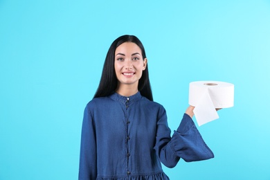 Beautiful woman holding toilet paper roll on color background