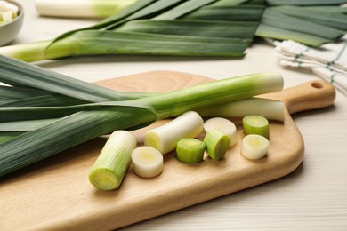 Photo of Whole and cut fresh leeks on white wooden table, closeup