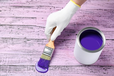 Woman making brush stroke with violet paint on pink wooden table, closeup. Space for text