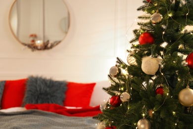 Photo of Beautiful decorated Christmas tree with fairy lights in bedroom, space for text. Interior design