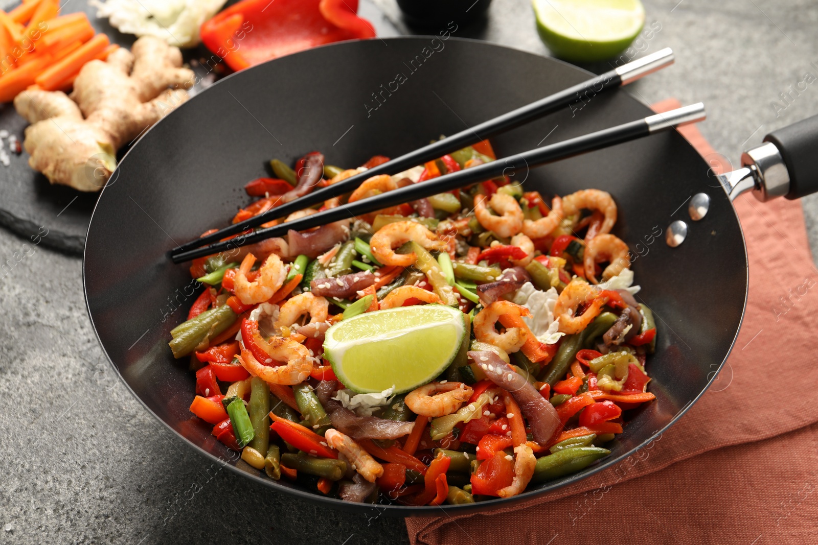 Photo of Shrimp stir fry with vegetables in wok and chopsticks on grey table