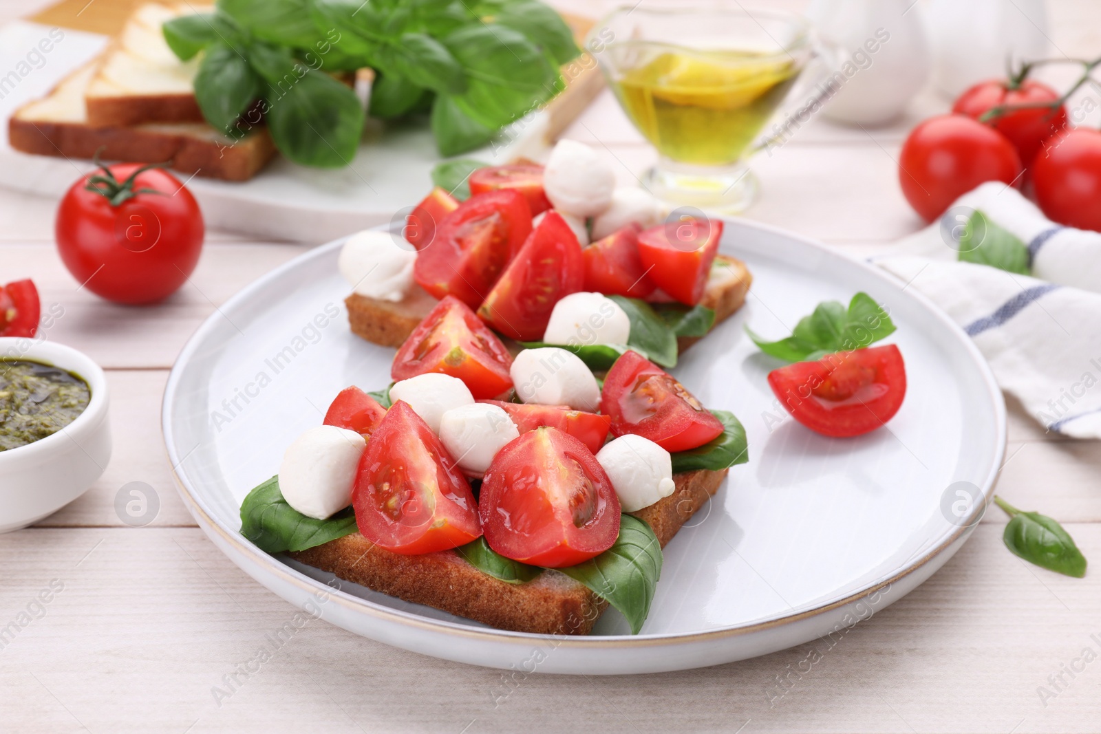 Photo of Delicious Caprese sandwiches with mozzarella, tomatoes, basil and pesto sauce on white wooden table