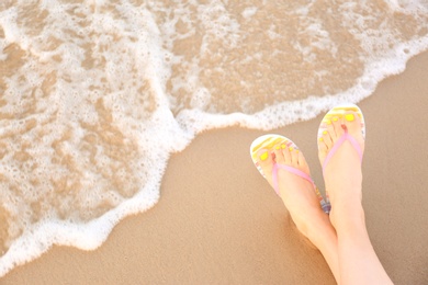 Photo of Closeup of woman with stylish flip flops on sand near sea, space for text. Beach accessories